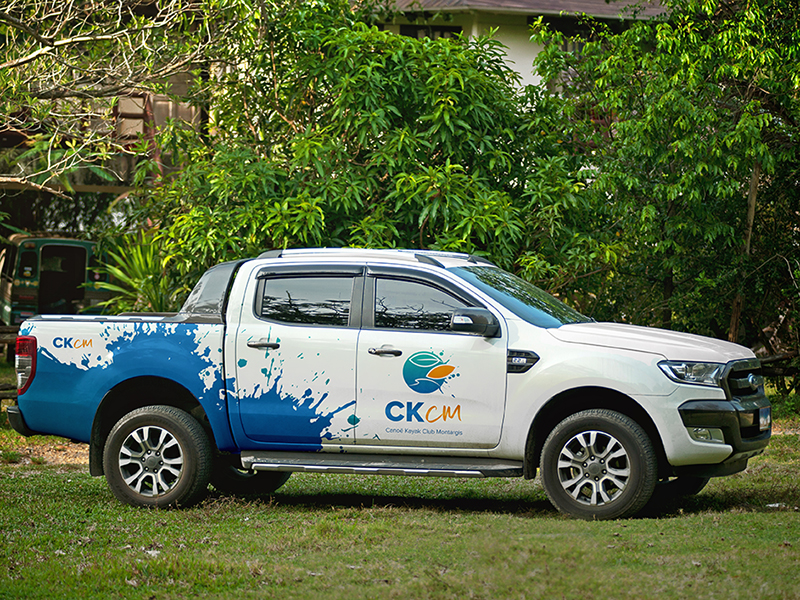 Simulation de marquage publicitaire (mockup) sur le profil d'un véhicule pick-up blanc, floqué avec l'identité visuelle bleue et le logo du CKCM.